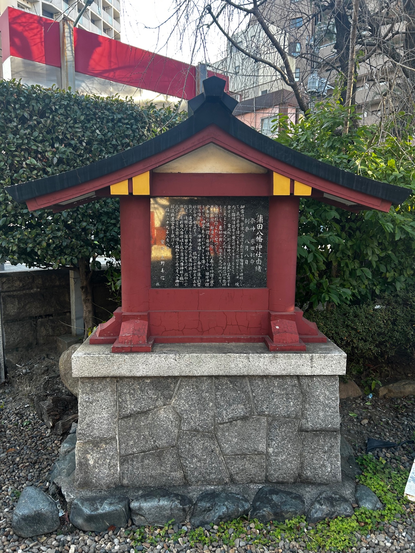 Small red and black wooden shrine with a stone foundation